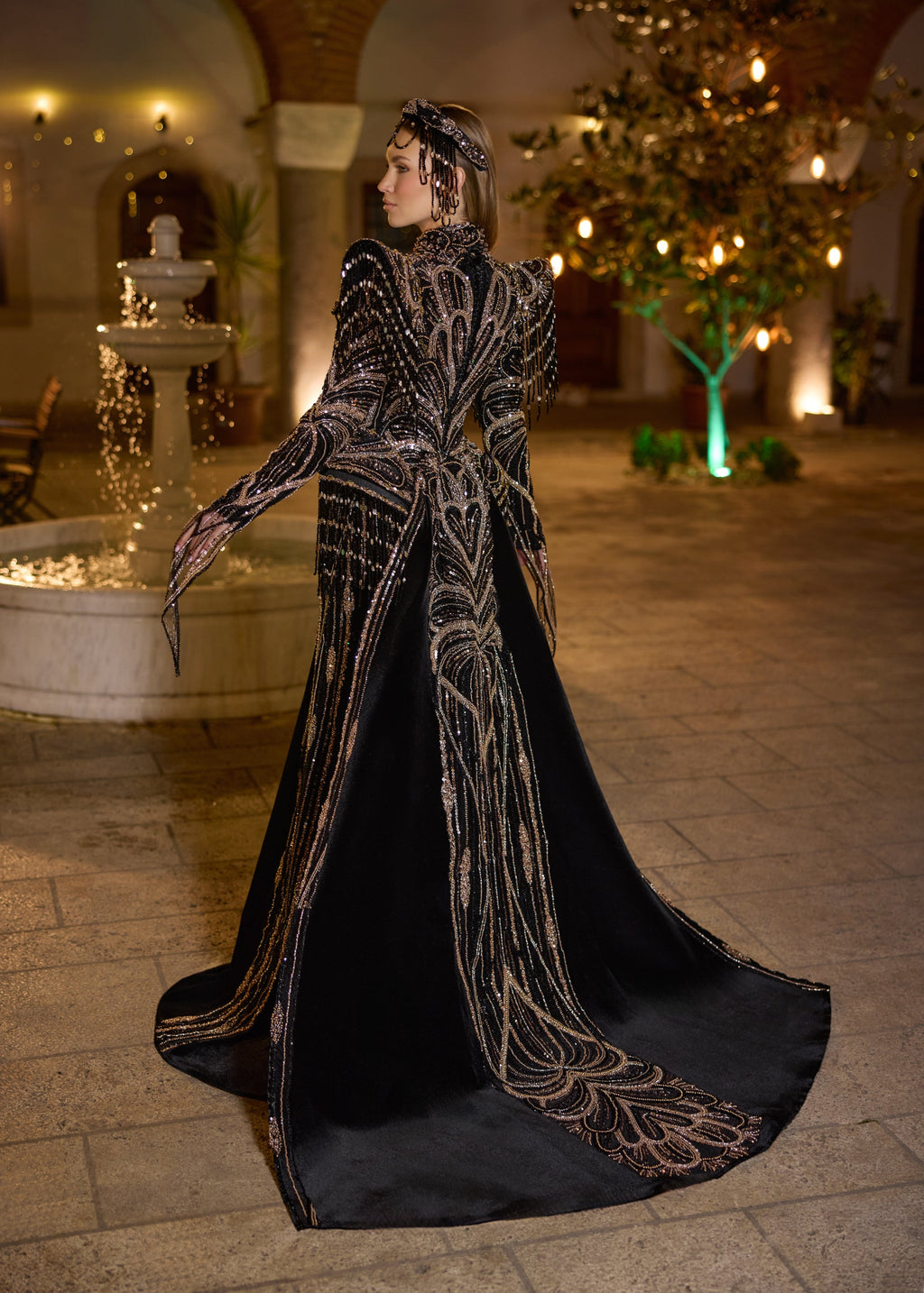 Full-length back view of the black velvet evening dress, highlighting the premium figure-hugging panel structure and the majestic sweeping royal train lavishly embroidered with shimmering metallic motifs.