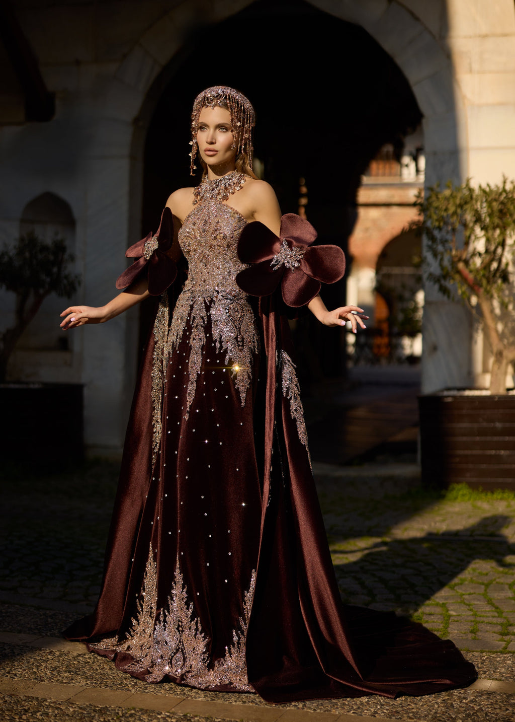 Medium shot of an exquisite velvet henna gown showcasing the symmetrical 3D velvet flowers on the sleeves, a hand-beaded rose gold bodice, and a luxury metallic crown.