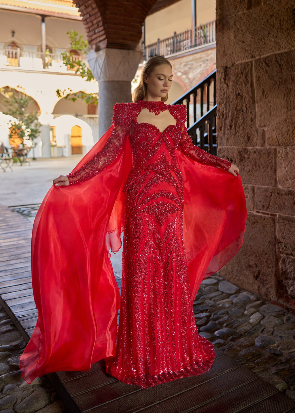 Full-length front view of a majestic red sequin mermaid Turkish henna dress with a dramatic flowing organza cape, padded shoulders, and a hand-beaded high-neck collar by Sultan Dress.