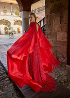 Back view of a luxury crimson red sequin wedding dress showing the open back design, sweeping train, and wind-blown flowing red organza cape.