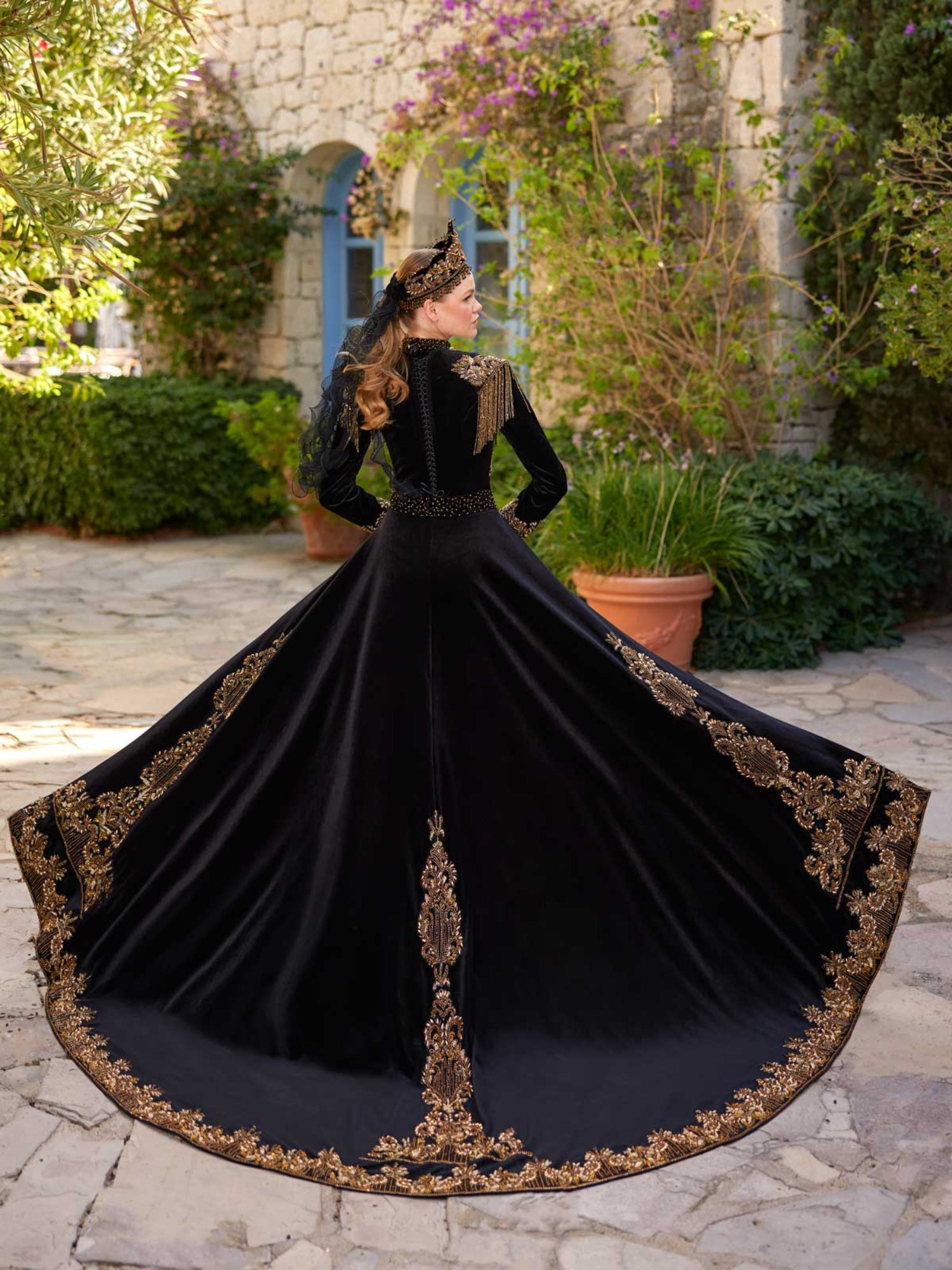Rear wide view showing the sweeping black velvet A-line skirt with gold lace border embroidery on the henna gown.