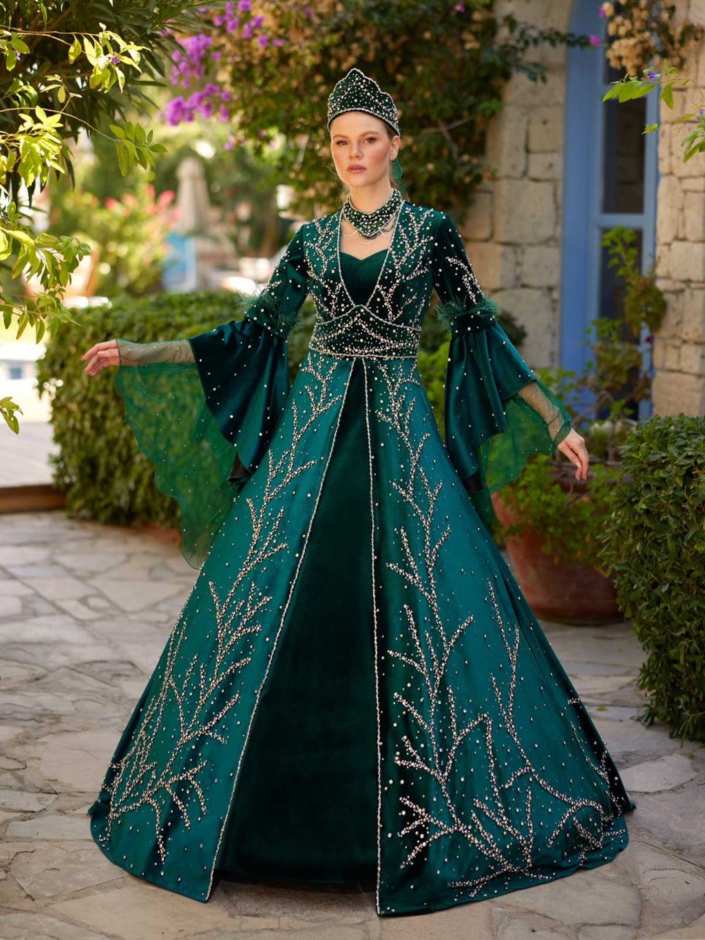 Full-length front view of the emerald green rhinestone embellished long frill sleeve henna dress with matching crown by Sultan Dress.