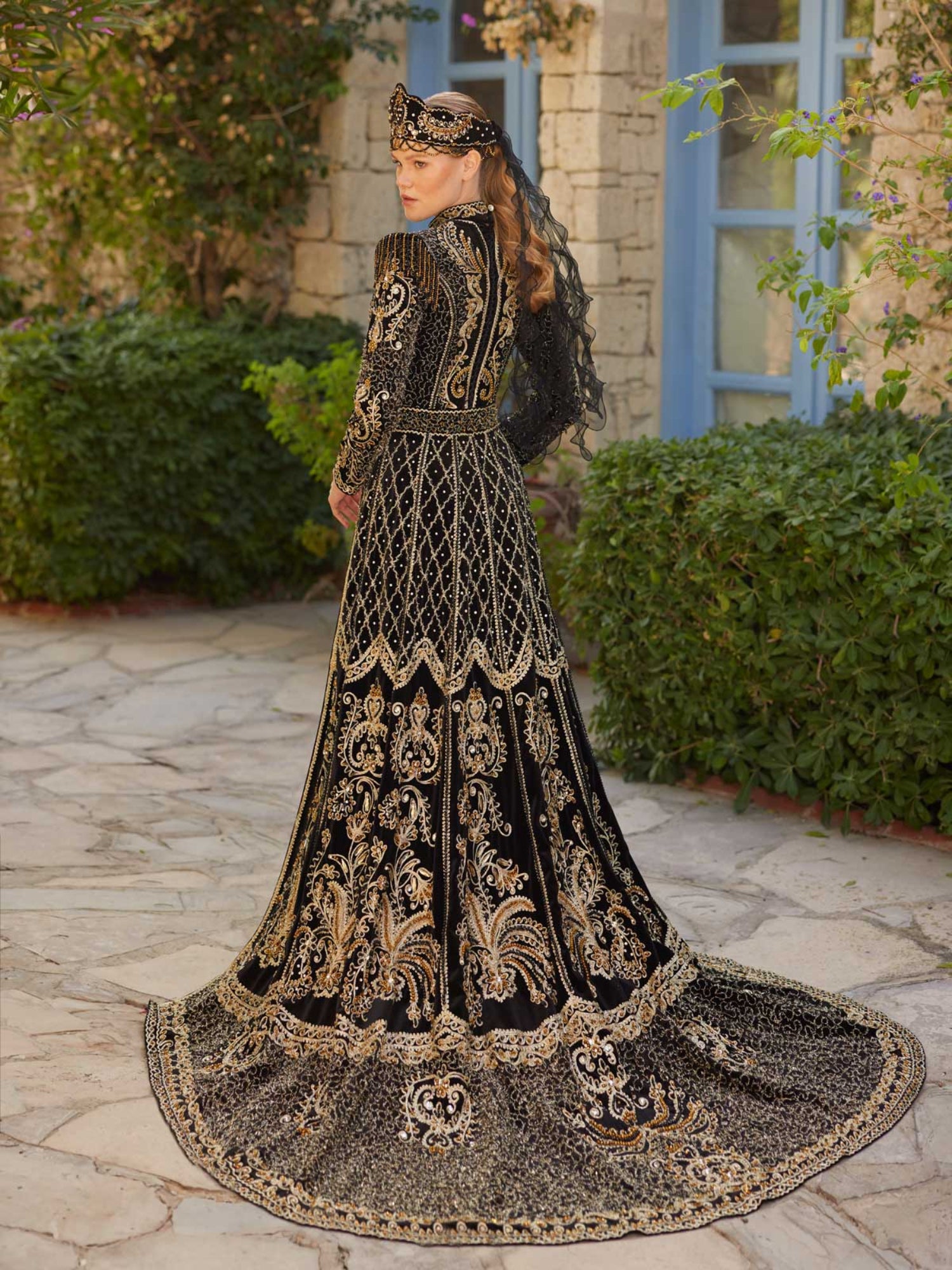 Rear view showing the dramatic gold-embroidered train and high collar on the black velvet modest henna dress.