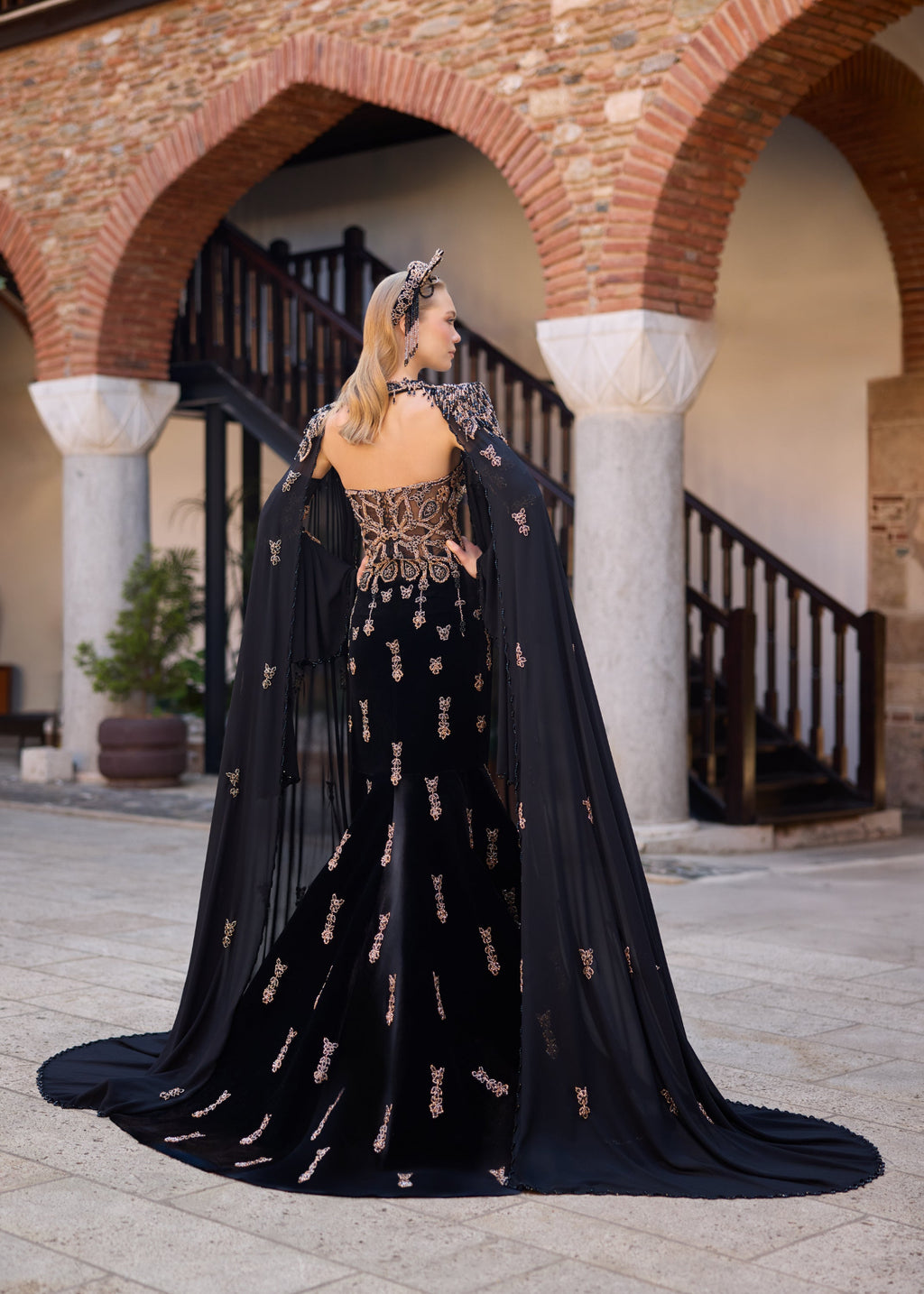Ottoman-inspired velvet henna dress with dramatic floor-length tulle cape sleeves and a fitted mermaid silhouette.