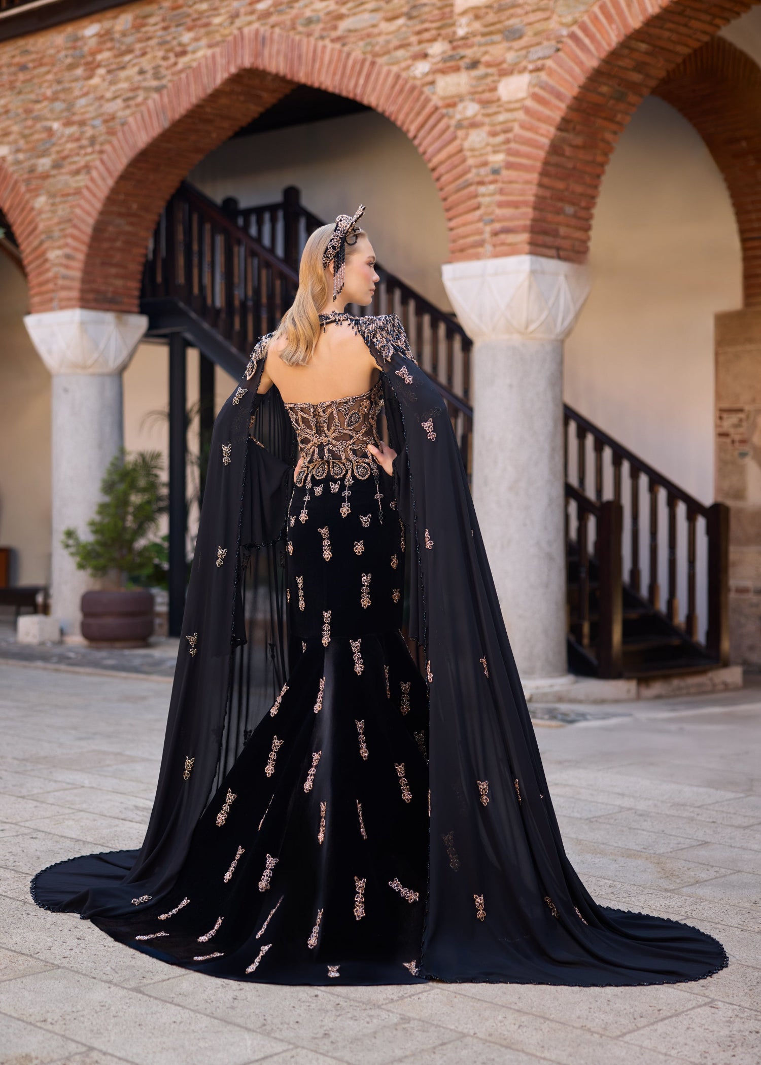 Ottoman-inspired velvet henna dress with dramatic floor-length tulle cape sleeves and a fitted mermaid silhouette.