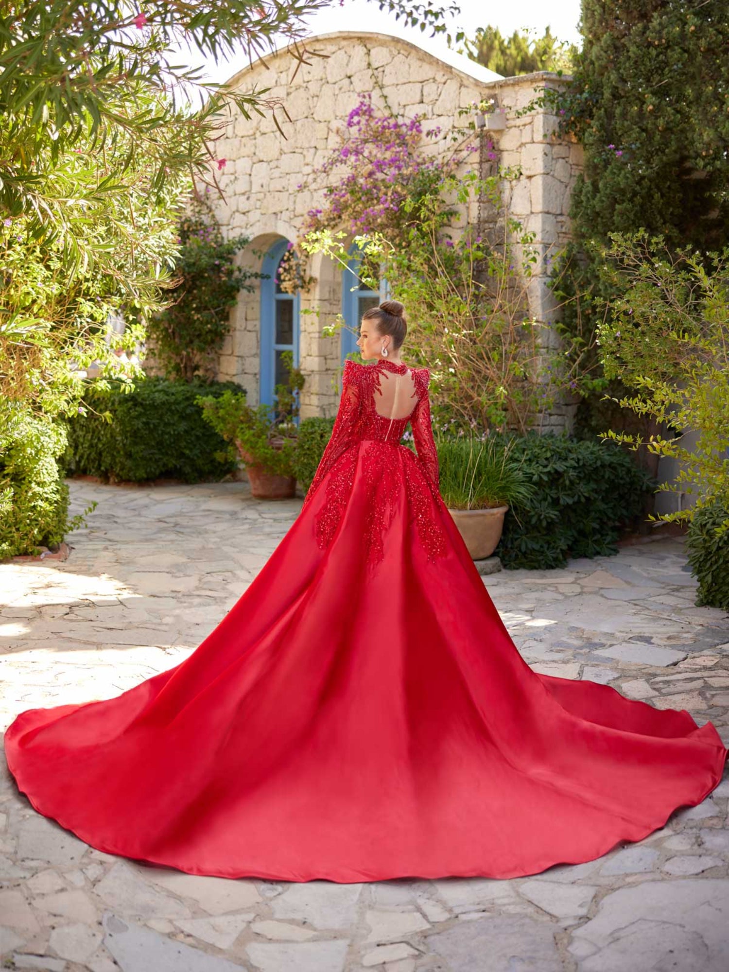 Rear view showing the dramatic detachable red satin overskirt train and illusion open back on the red beaded mermaid dress.