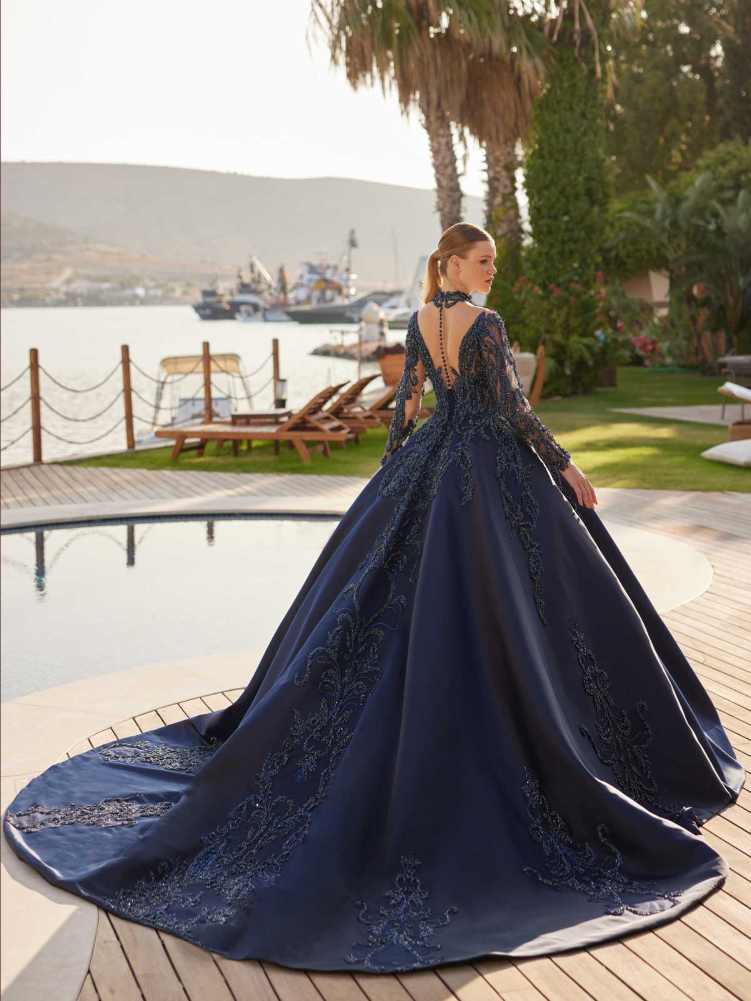 Rear view showcasing the open illusion back and sweeping cathedral train of the navy blue beaded princess ball gown by Sultan Dress.