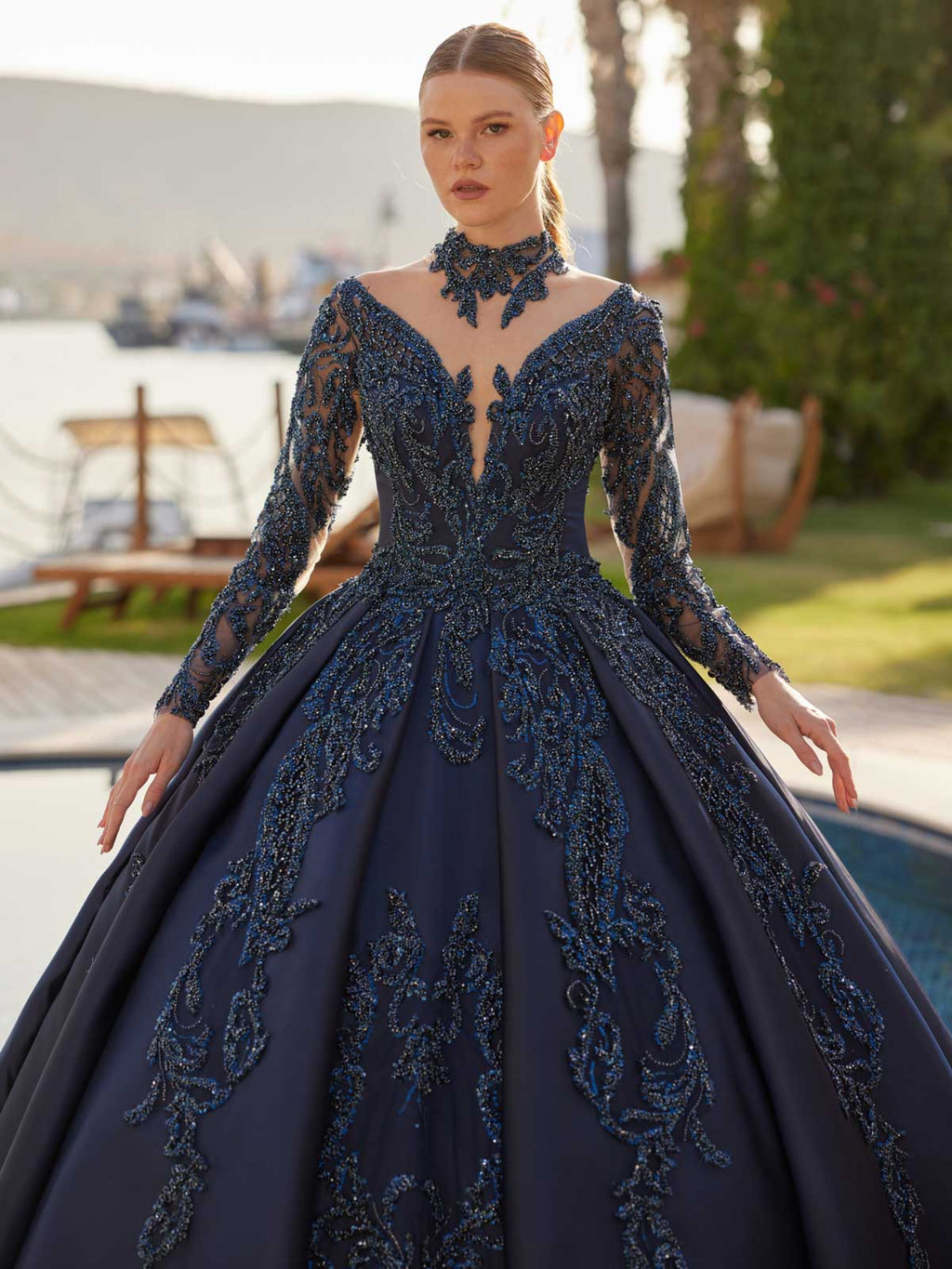 Close-up view of the plunge v-neckline, beaded choker collar, and long illusion sleeves on the midnight navy gown.