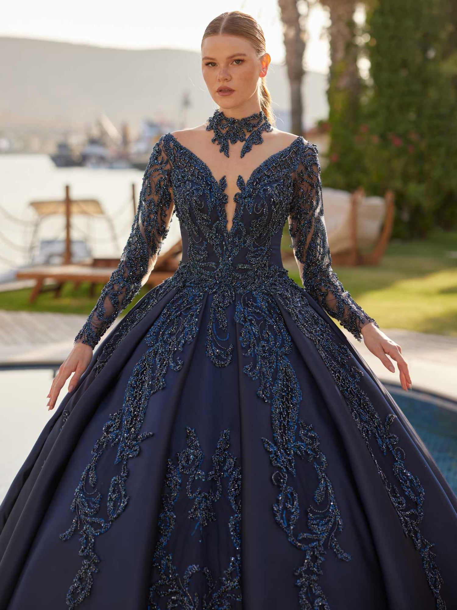 Close-up view of the plunge v-neckline, beaded choker collar, and long illusion sleeves on the midnight navy gown.
