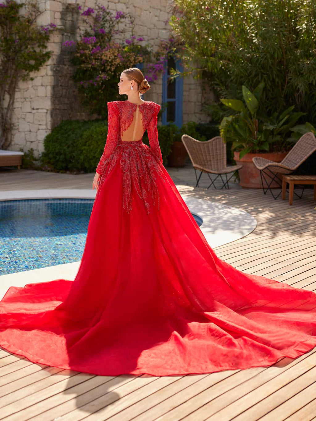 Rear side view highlighting the dramatic sweeping red tulle train overskirt and beaded back of the long-sleeve evening gown.
