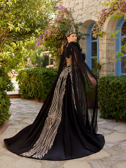 Rear view showing the dramatic flowing tulle shoulder cape and fitted back pattern of the black velvet gold sequin henna dress.