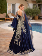 Rear view showing the scoop back bodice, gold embroidered skirt train, and draped sheer navy cape on the velvet caftan gown.