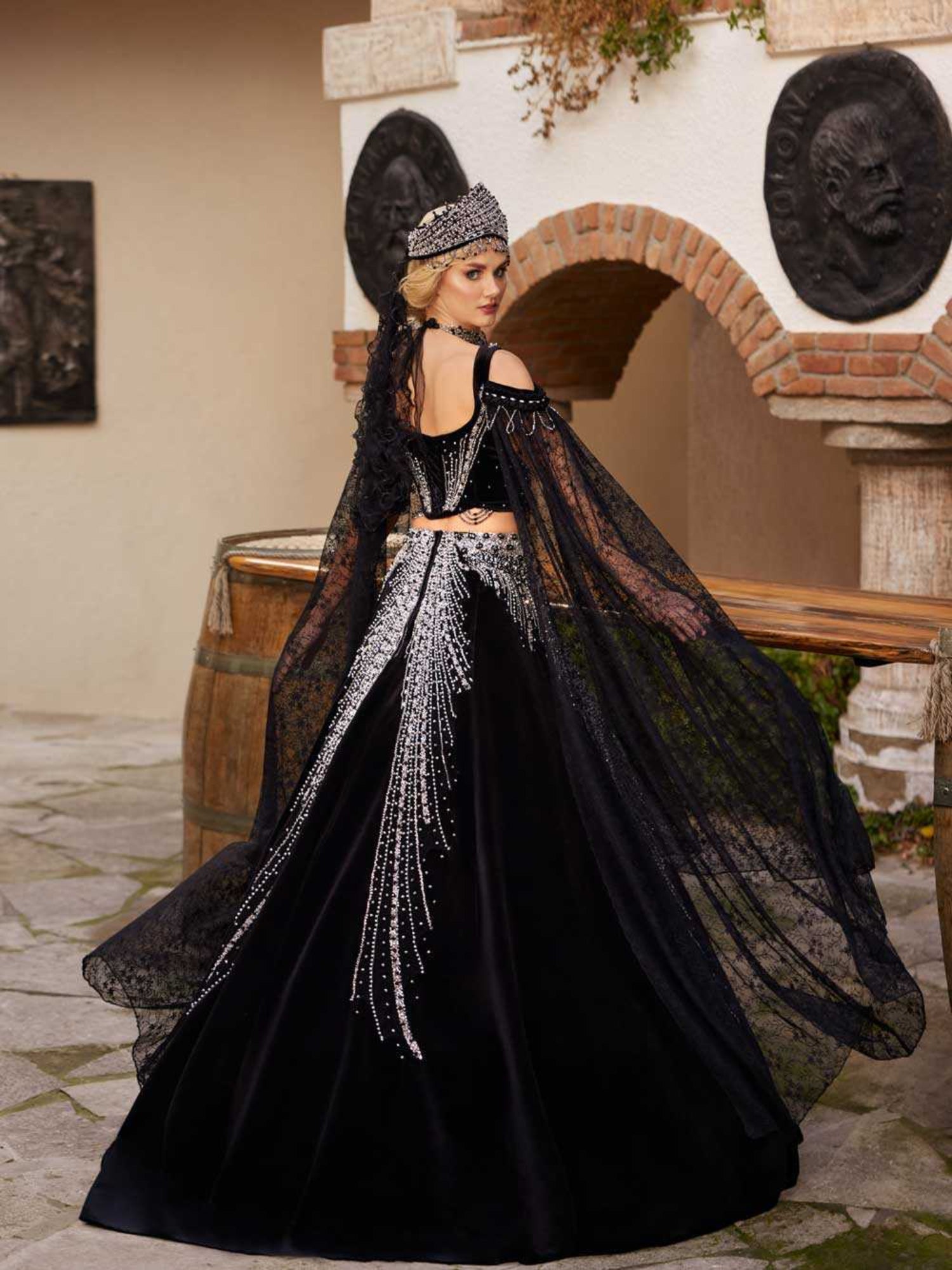 Rear view showing the two-piece black velvet beaded corset top, open back, silver embroidery, and long lace cape sleeves by Sultan Dress.