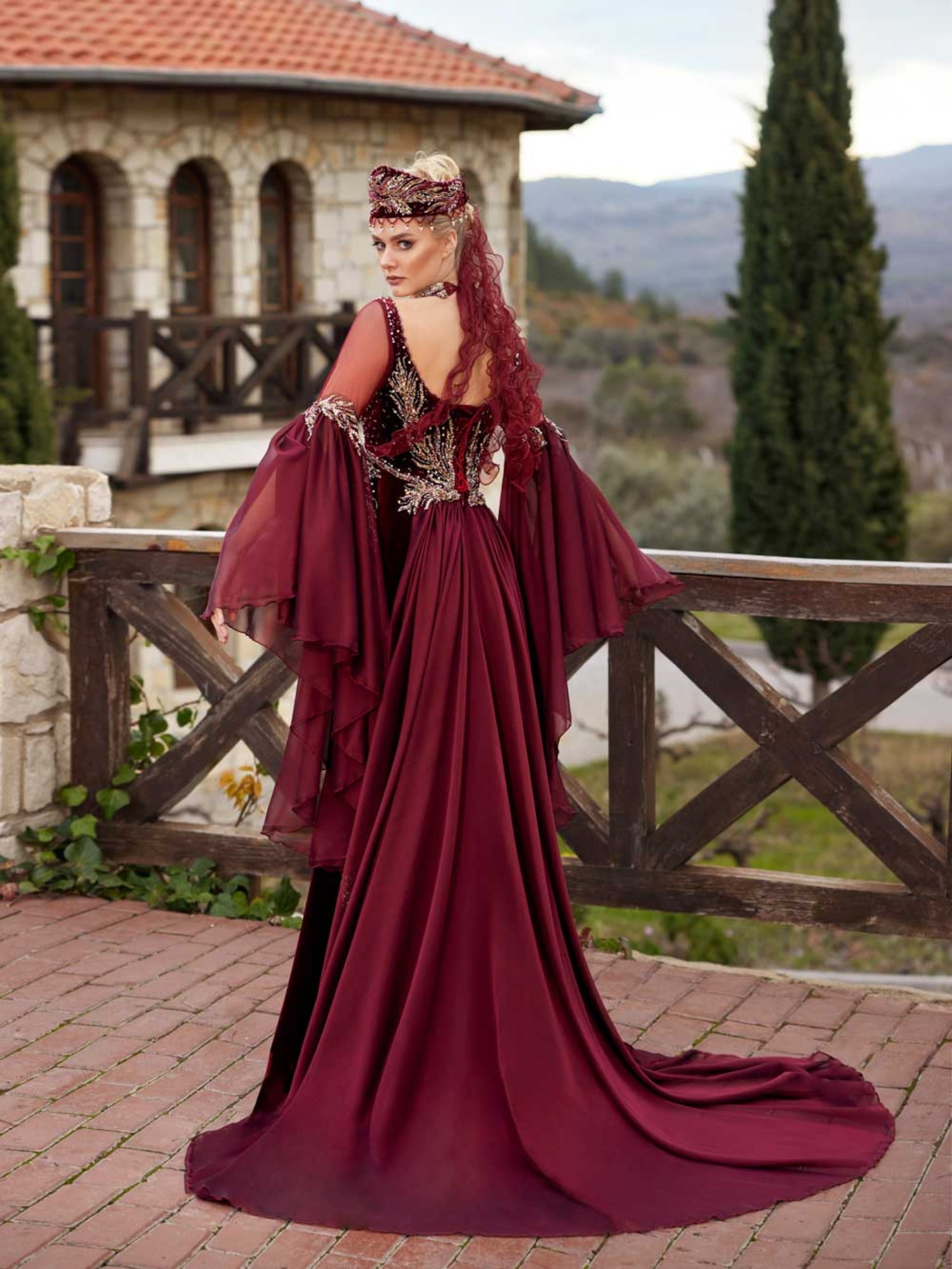 Rear view showing the gold-embroidered velvet bodice, sheer back detail, and sweeping burgundy chiffon rear train.