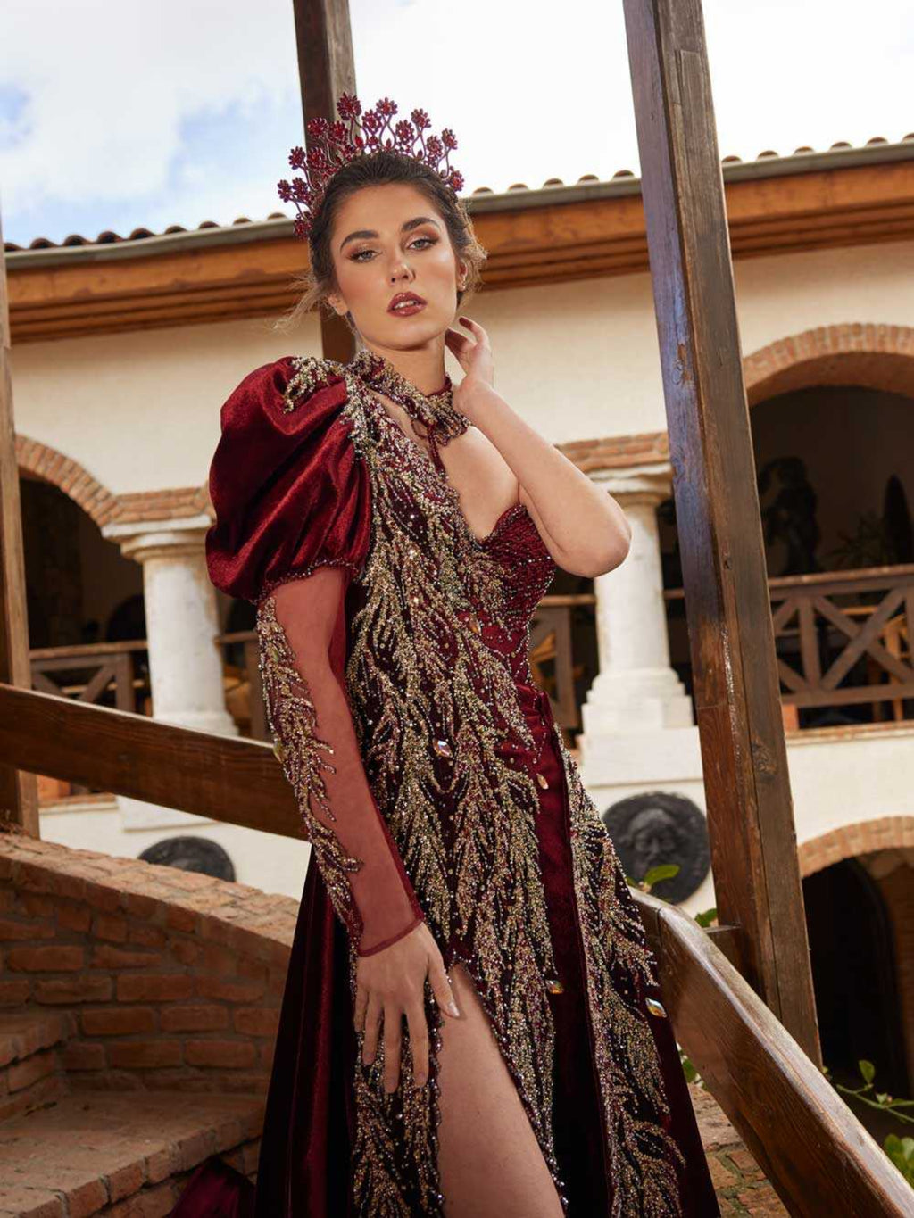 Front view of the burgundy velvet one-shoulder engagement gown featuring metallic gold leaf embroidery, high slit, and illusion sleeve by Sultan Dress.