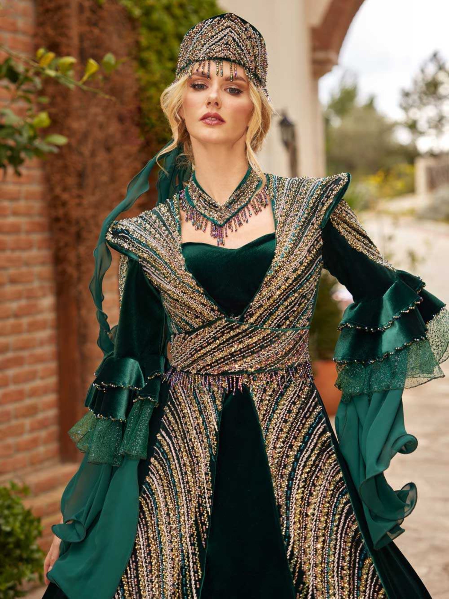 Close-up of the handcrafted gold bead lines, beaded collar necklace, and tiered chiffon sleeve ruffles on the dark green velvet gown.