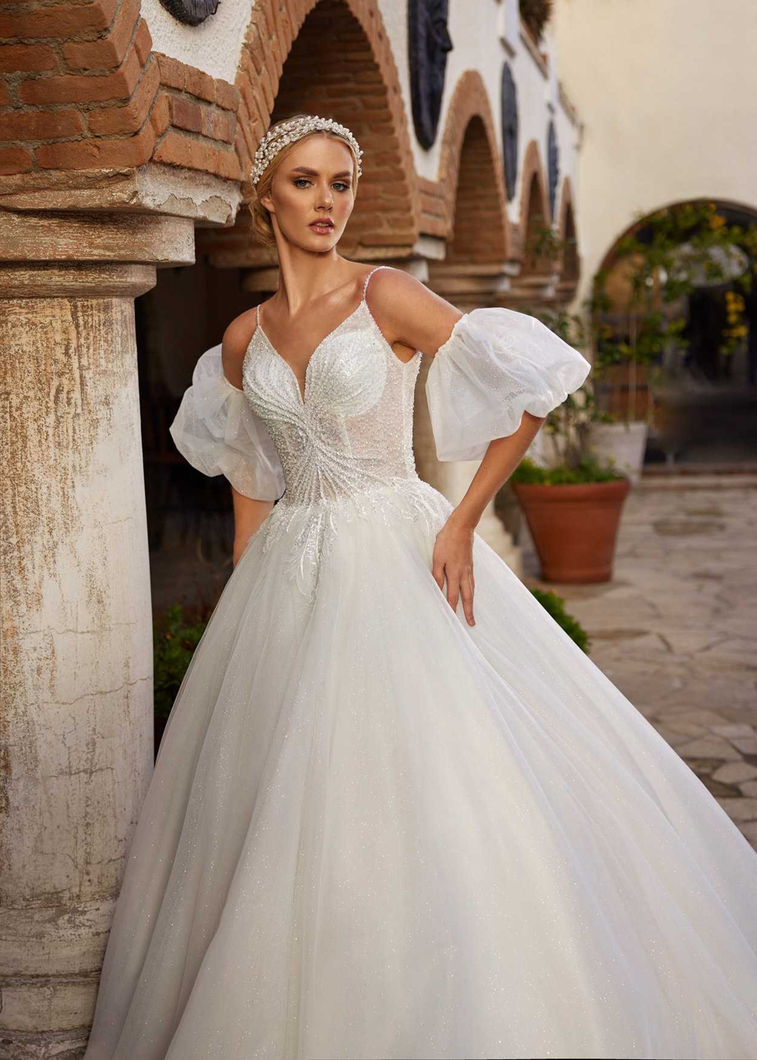 Rear view showing the low V-back, detachable puff sleeves, and shimmering tulle chapel train of the wedding gown.