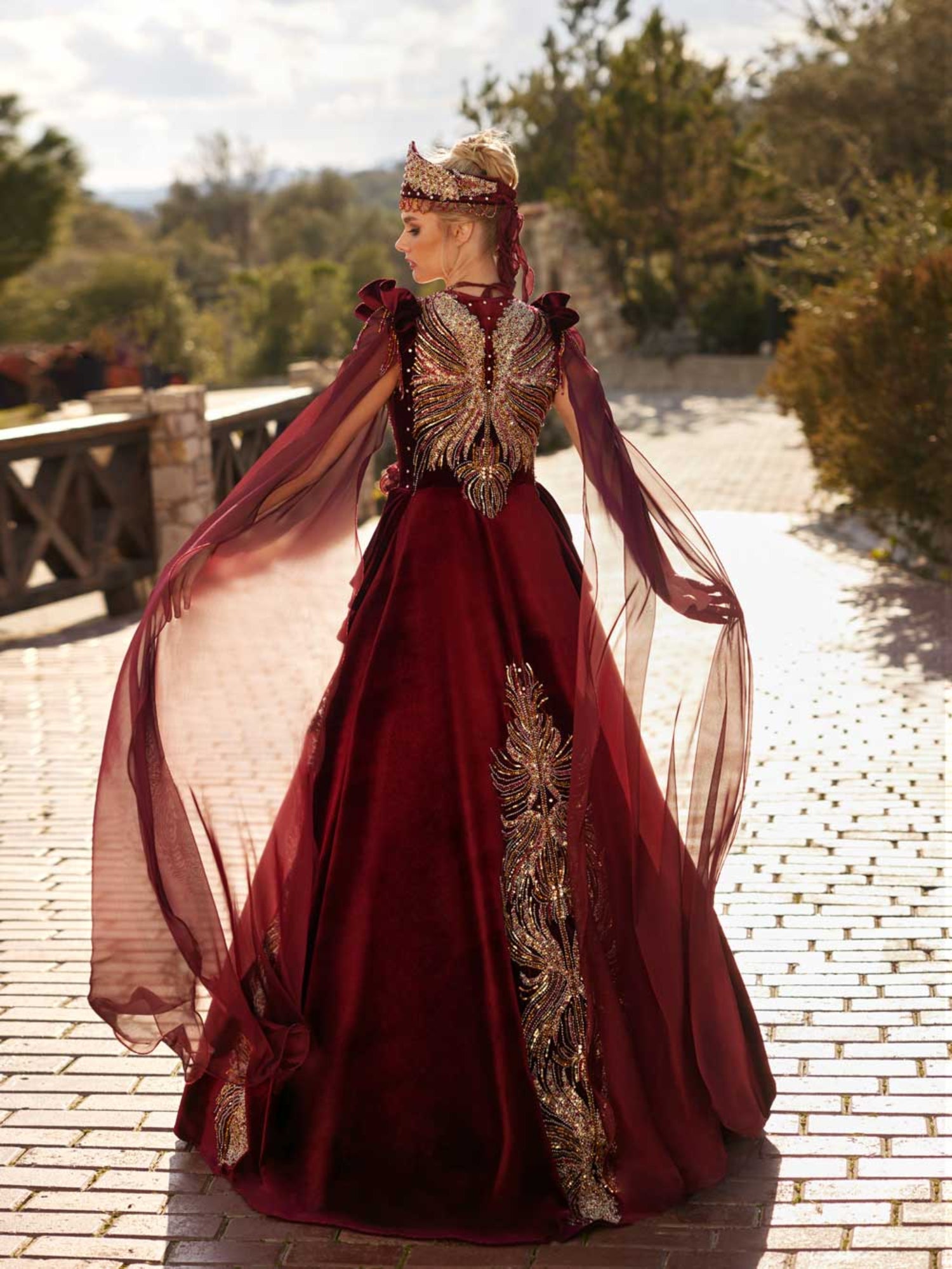 Rear view showcasing the colorful crystal beaded butterfly wing back embroidery and floor-length tulle cape sleeves on the maroon velvet Henna dress by Sultan Dress.