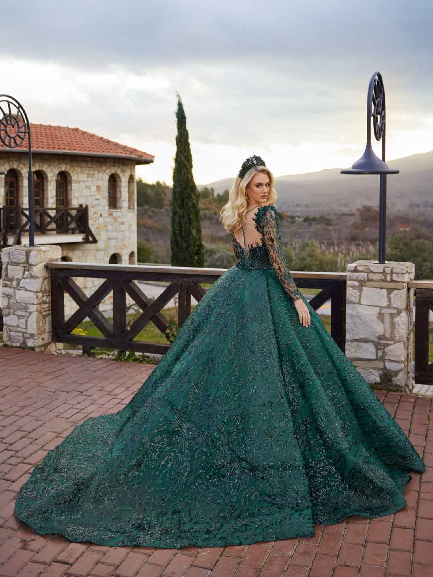 Rear view highlighting the sheer lace illusion back, long sleeves, and sweeping sequined train on the emerald green ball gown.