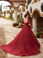 Front full-length view of the maroon A-line tulle ball gown featuring a beaded sweetheart corset bodice and sheer puff sleeves by Sultan Dress