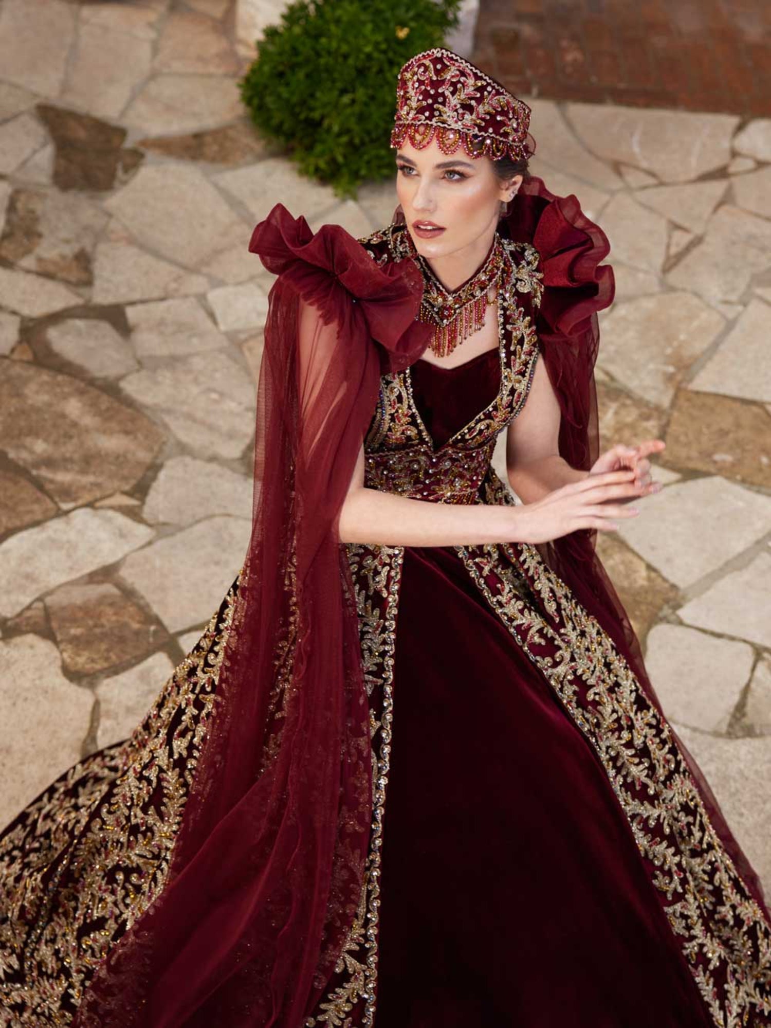 Front view of the maroon velvet Turkish Henna kaftan gown with all-over gold sequin lace embroidery, sweetheart neck, and mesh cape sleeves by Sultan Dress.