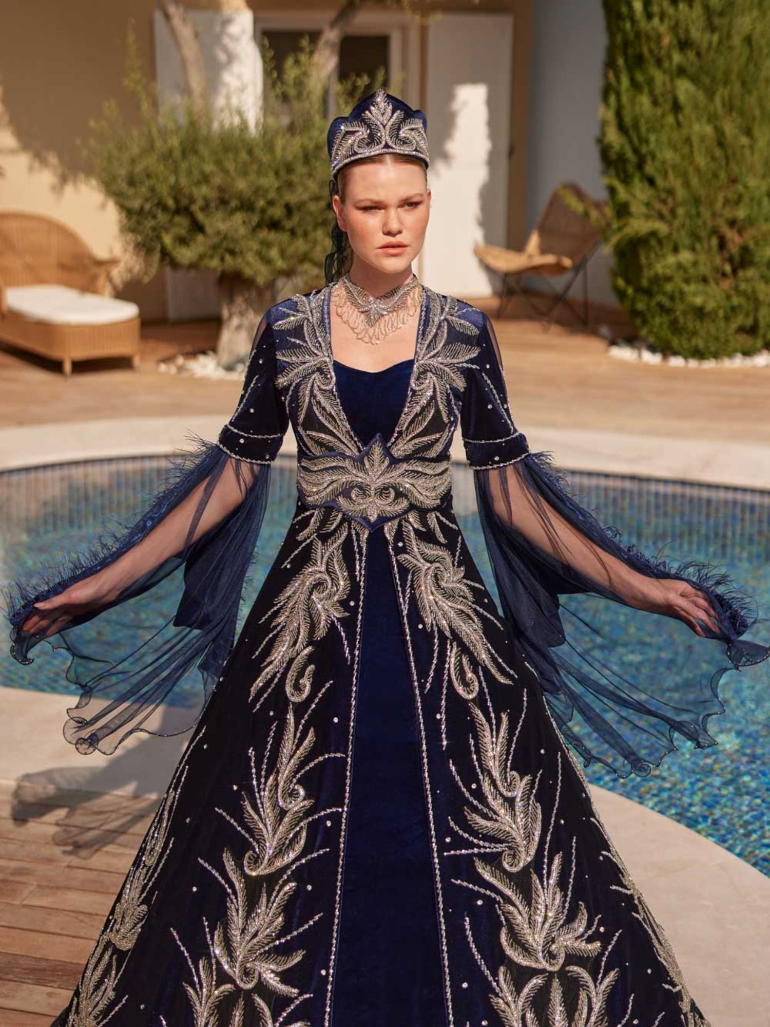 Rear view showing the silver embroidered back pattern, crystal scatter accents, and veil accessory on the royal blue velvet Henna gown.