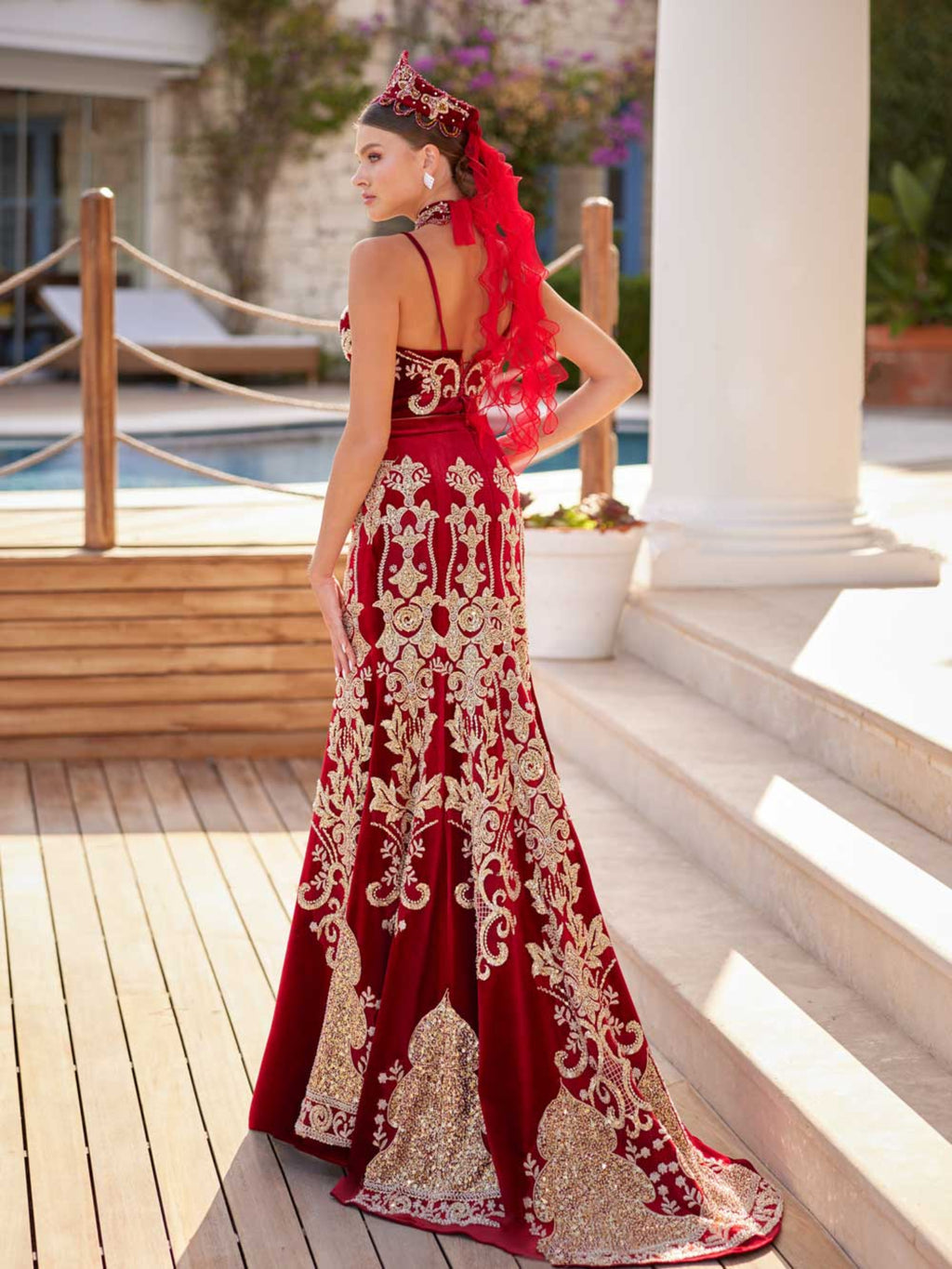 Rear view showing the gold filigree embroidered back of the skirt, red tulle veil attachment, and crown accessory on the red velvet Henna dress.