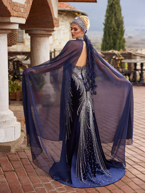 Rear view highlighting the open back design, beaded halter collar, and sweeping sheer cape of the custom navy formal dress.