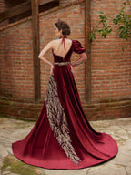 Rear view showing the open back detail, choker neck tie, and sweeping gold-embroidered train on the burgundy velvet evening gown.