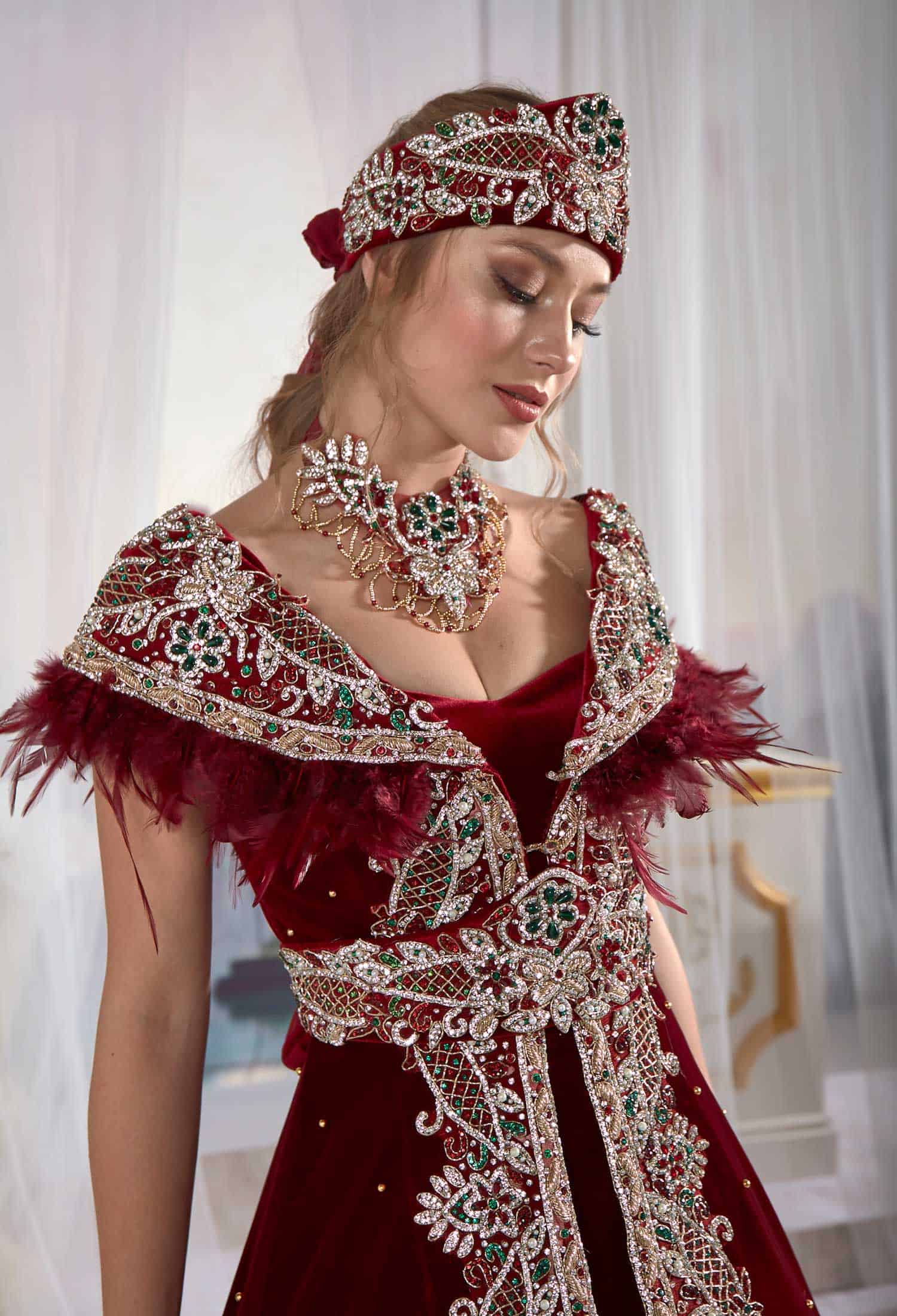 Close-up detail view of the artisan delicate beadwork and soft drape velvet texture on the red and navy caftan gown.
