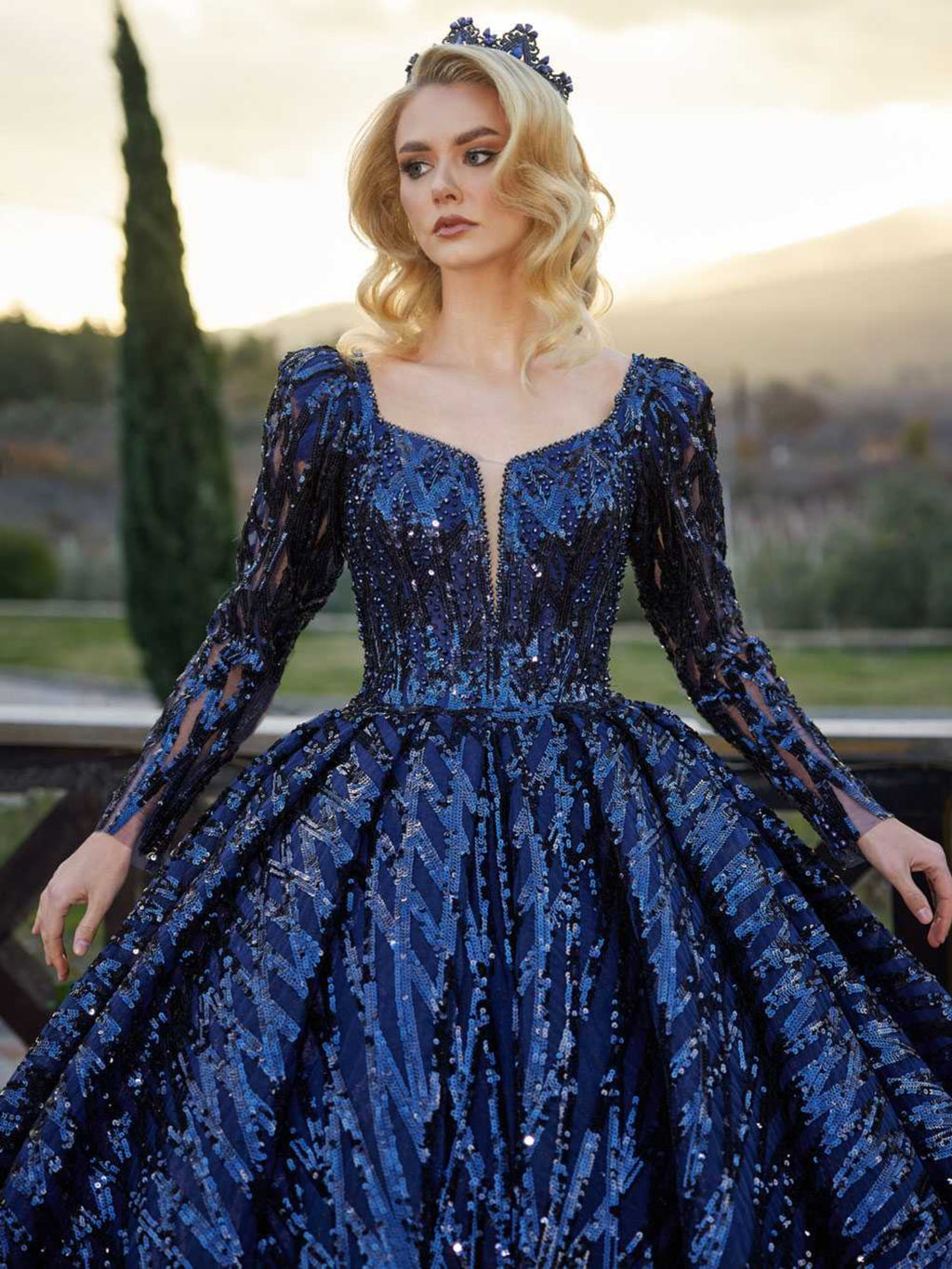 Full-length front view showing the long sleeve heavily sequined royal blue ball gown with a plunge neckline by Sultan Dress.
