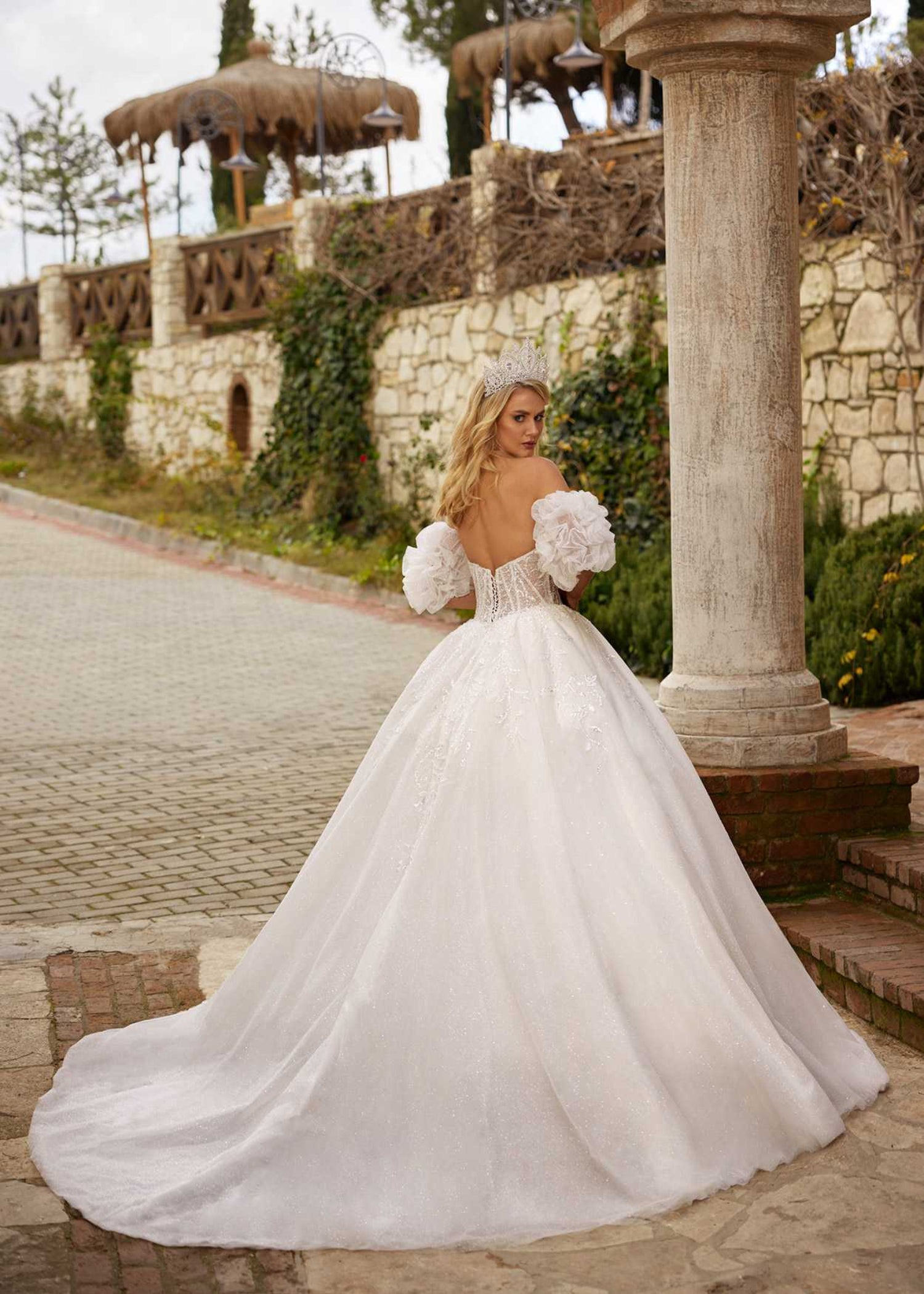 Rear view showing the lace-up corset back, dramatic ruffled sleeves, and sparkling tulle train of the ball gown.