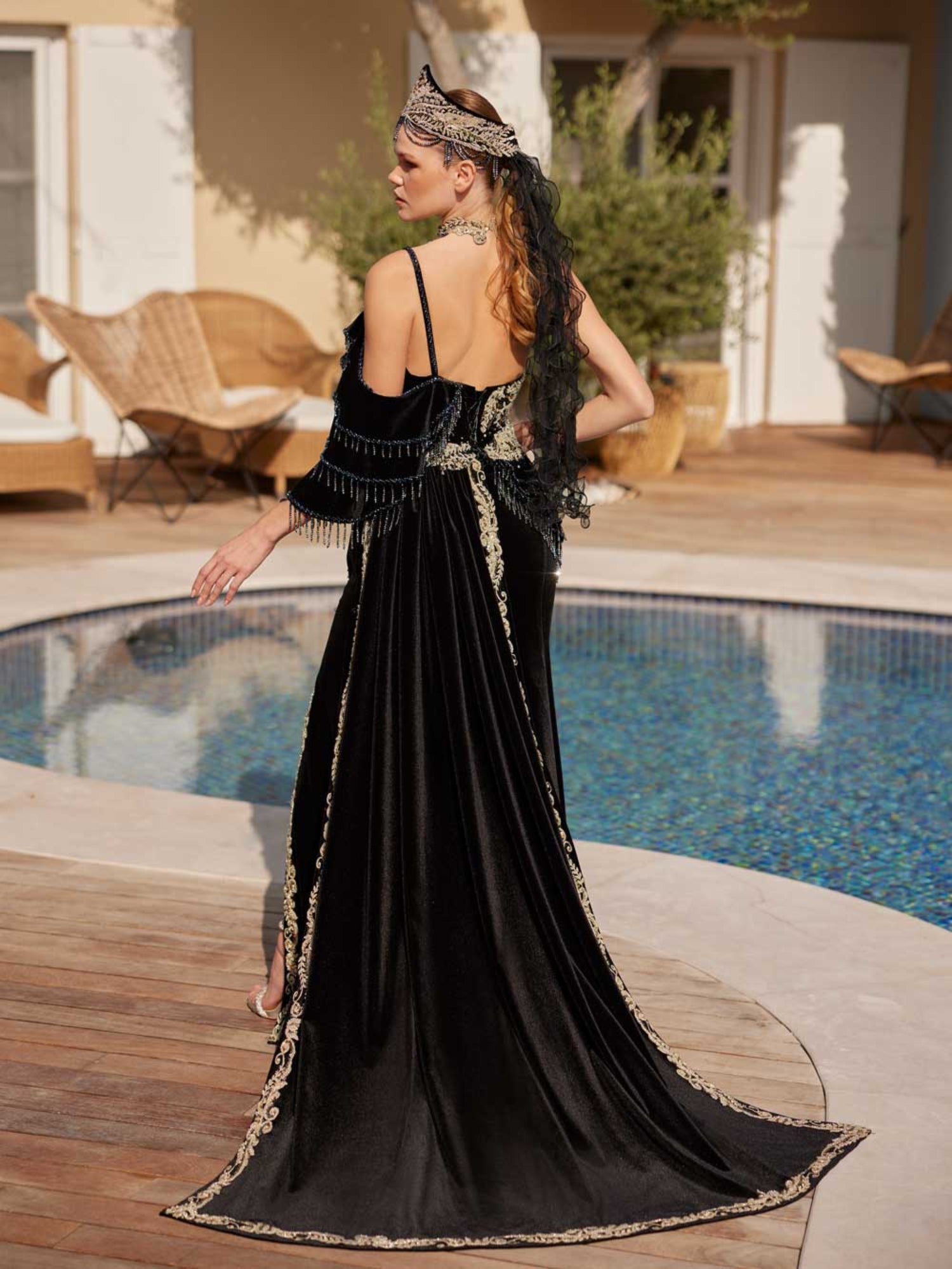 Rear view showing the thin spaghetti strap, scoop back, and sweeping gold lace bordered train on the black velvet mermaid gown.