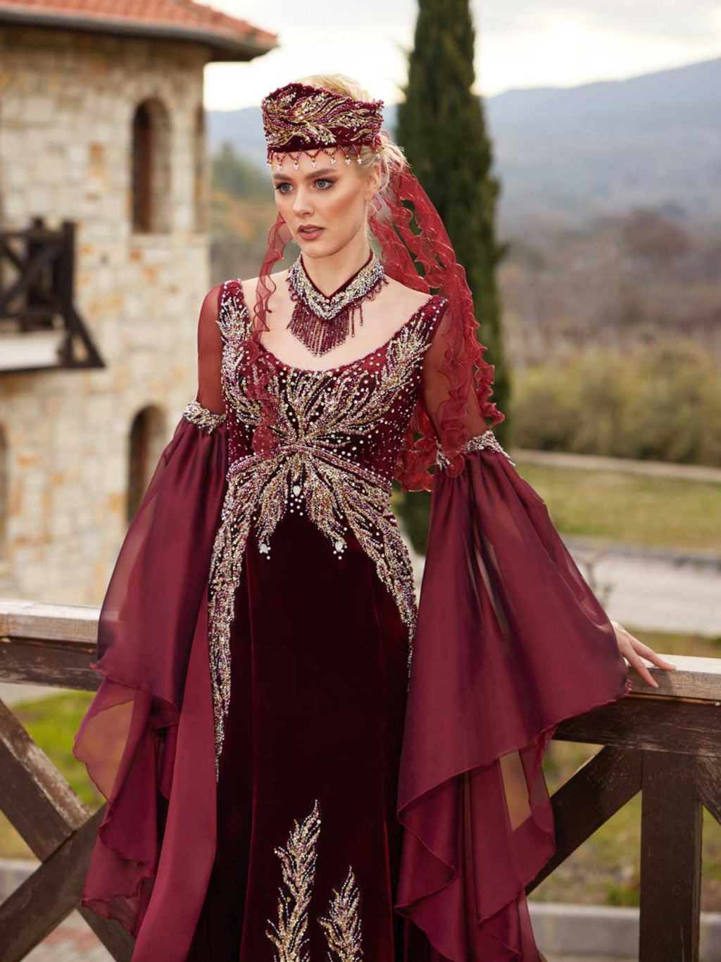 Front view of the fitted burgundy velvet evening dress with gold lace sunburst embroidery, V-neckline, and draped chiffon sleeves by Sultan Dress.